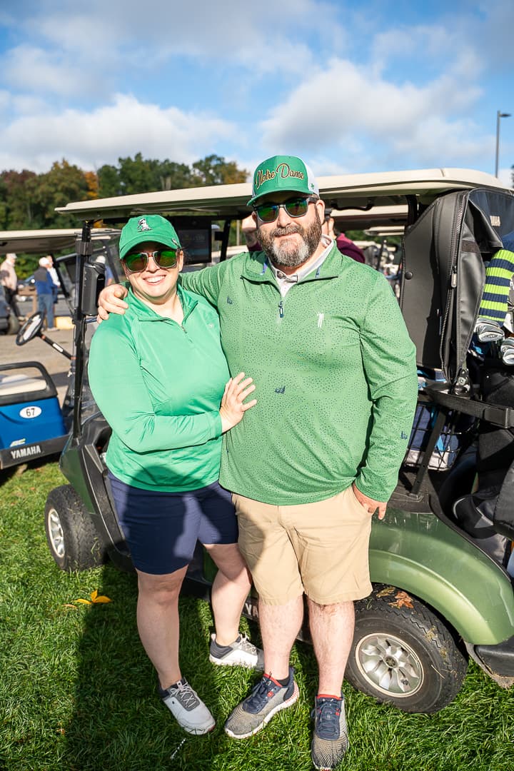 Two participants smiling beside a golf cart at the Live Like Brent Classic.