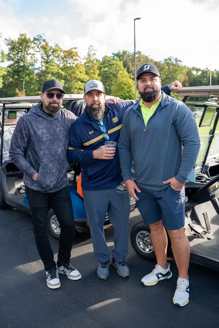 Three golfers posing beside golf carts at the Live Like Brent Classic.